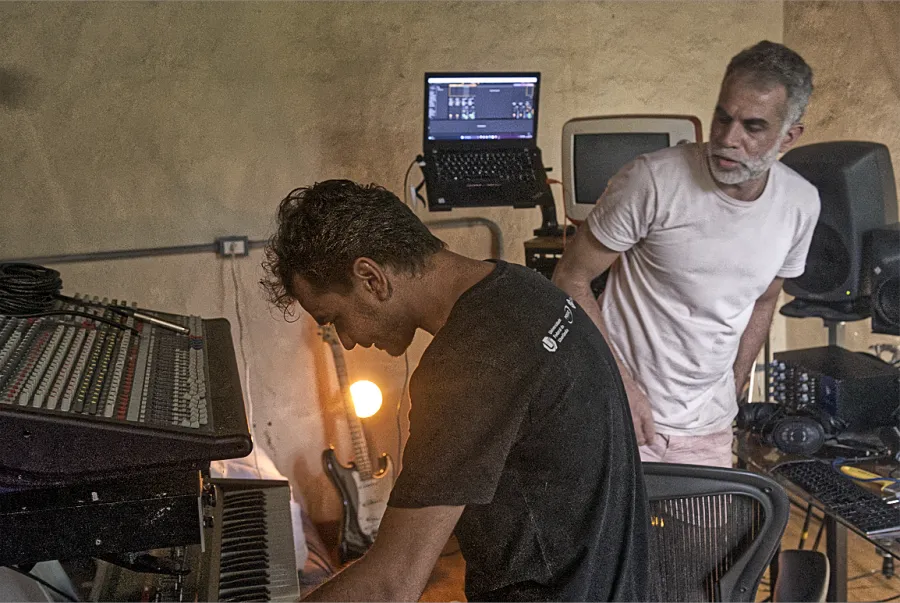Two collaborators working together around instruments and studio equipment